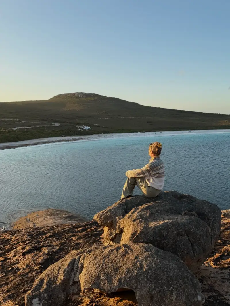 Michaela sitzt auf einem Felsen mit Blick auf die Lucky Bay im Abendlicht